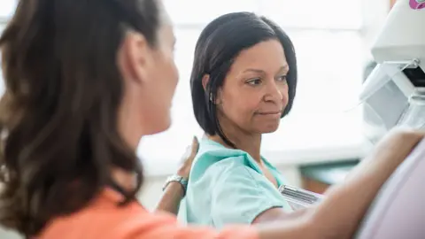 Getty Images A woman goes for a mammogram. She is pictured alongside a female medical professional.