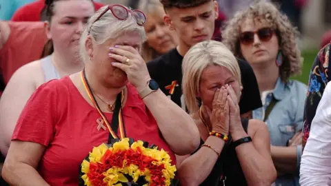 PA Two tearful women are pictured as part of a group which held a minute's silence in May 2024 in memory of people who died because of the infected blood scandal. They are covering their faces with their hands in grief.