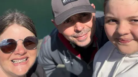 Jenni Whitmore A selfie of Jenni with her husband Gareth and young daughter Carys. Jenni has her hair tied back an is wearing sunglasses. Her husband and daughter are wearing grey hoodies. Her husband is wearing a grey baseball cap.