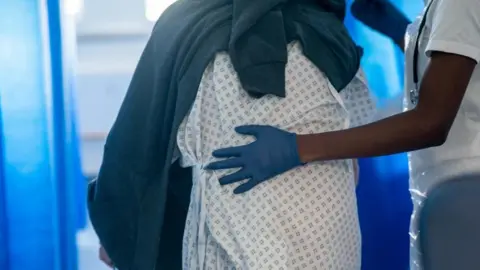 PA Image shows a patient being led by a member of staff on a NHS hospital ward at Ealing Hospital in London
