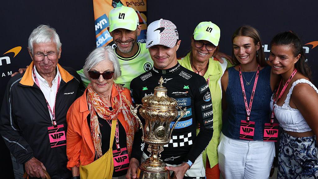 Lando Norris poses with the British Grand Prix winner's trophy with his grandparents, parents and sisters at Silverstone