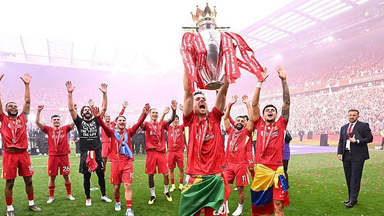 Diogo Jota lifting the Premier League title above his head in red Liverpool kit