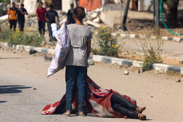 A Palestinian girl stands over the covered body of a person who was killed seeking food at a Gaza Humanitarian Foundation distribution point in central Gaza's Nuseirat camp, on Aug. 4, 2025.