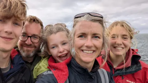 Family handout Family photo of Wren with the sea in the background. from left to right we her brother, dad, wren, her mum and her sister. all are wearing raincoasts and smiling directly into the camera.