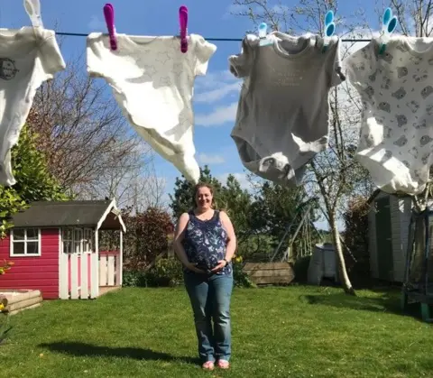 Lori - Mark Quate Jacqui, who is heavily pregnant, is wearing blue jeans and a blue vest top standing in a garden with a washing line in the foreground. The washing line has baby clothes pegged to it.