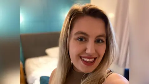 Lowri Puw Lowri Puw - a smiling woman with long blonde hair, wearing red lipstick.