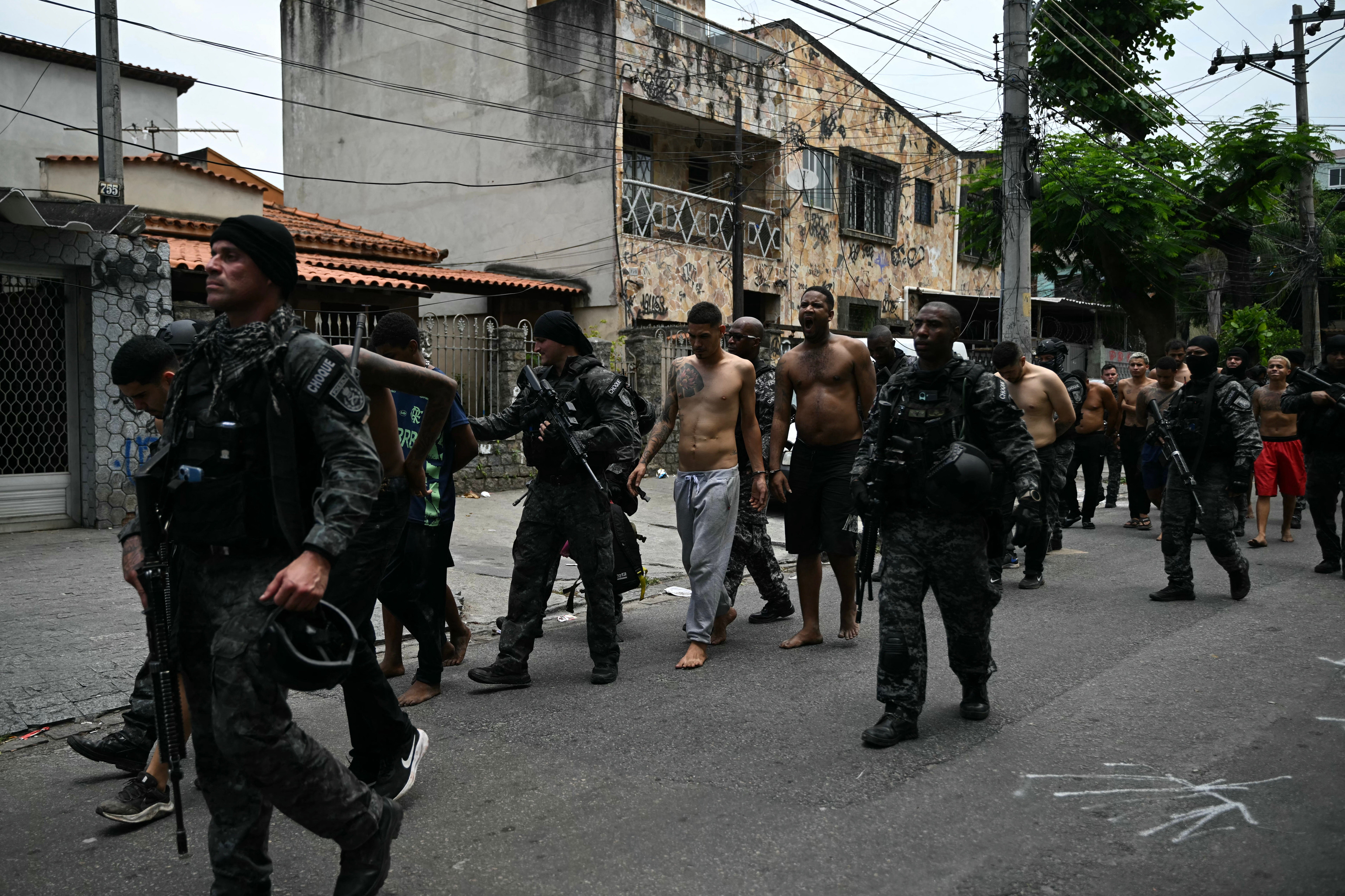 Police officers escort alleged criminal arrested during the Operacao Contencao (Operation Containment) at the Vila Cruzeiro favela, in the Penha complex, in Rio de Janeiro, Brazil, on October 28, 2025. At least 2,500 security forces agents took part in an operation to arrest drug traffickers from the Comando Vermelho (CV), which resulted in 64 people dead, authorities reported. (Photo by Mauro PIMENTEL / AFP) (Photo by MAURO PIMENTEL/AFP via Getty Images)