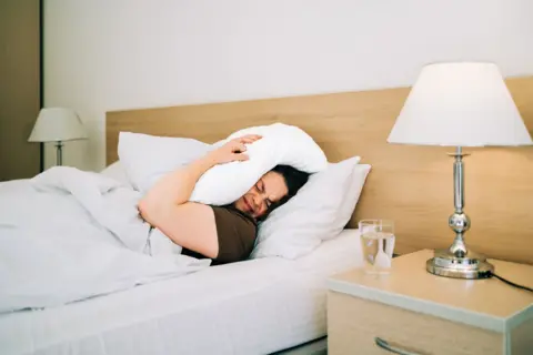 Getty Images Woman lying in bed with a pillow over her head