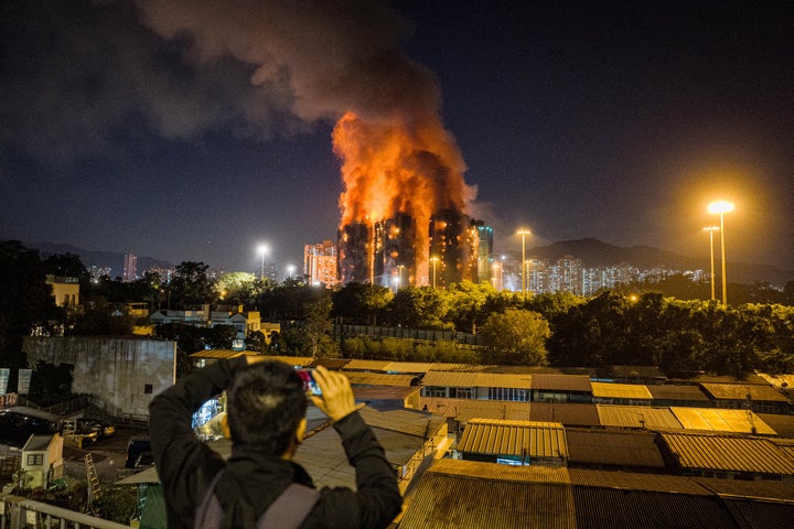 An onlooker takes photos as a major fire engulfs several apartment blocks at the Wang Fuk Court residential estate (background) in Hong Kong's Tai Po district on November 26, 2025. (Photo by AFP via Getty Images)
