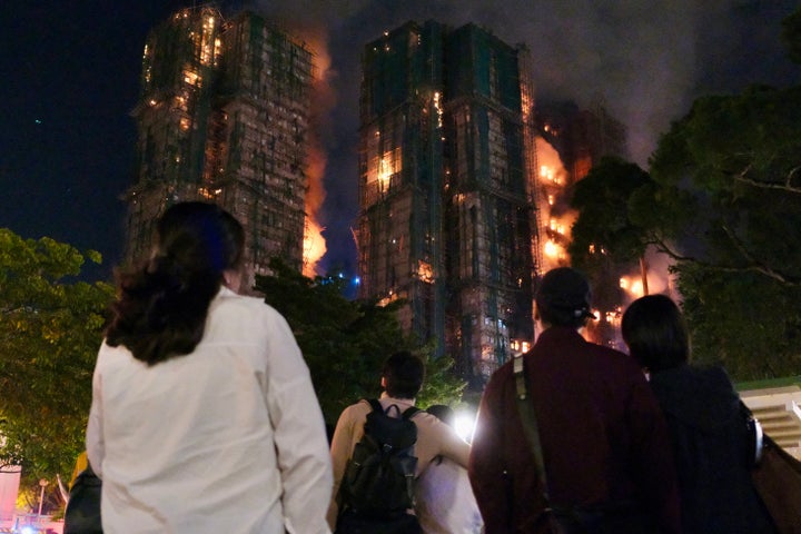 People look on as thick smoke and flames rise during a major fire at the Wang Fuk Court residential estate in Hong Kong's Tai Po district on November 26, 2025. (Photo by Tommy WANG / AFP via Getty Images)
