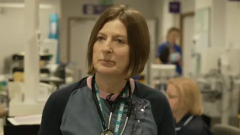BBC News Dr Alner, who has a stethascope around her neck, stands in the ward after seeing her patients