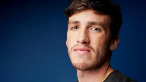 Family handout A young man with short dark hair and stubble looks directly at the camera in front of a dark blue background.