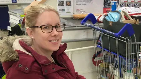 Rebecca Middleton A woman with blonde hair and glasses smiling wearing a red coat. 
