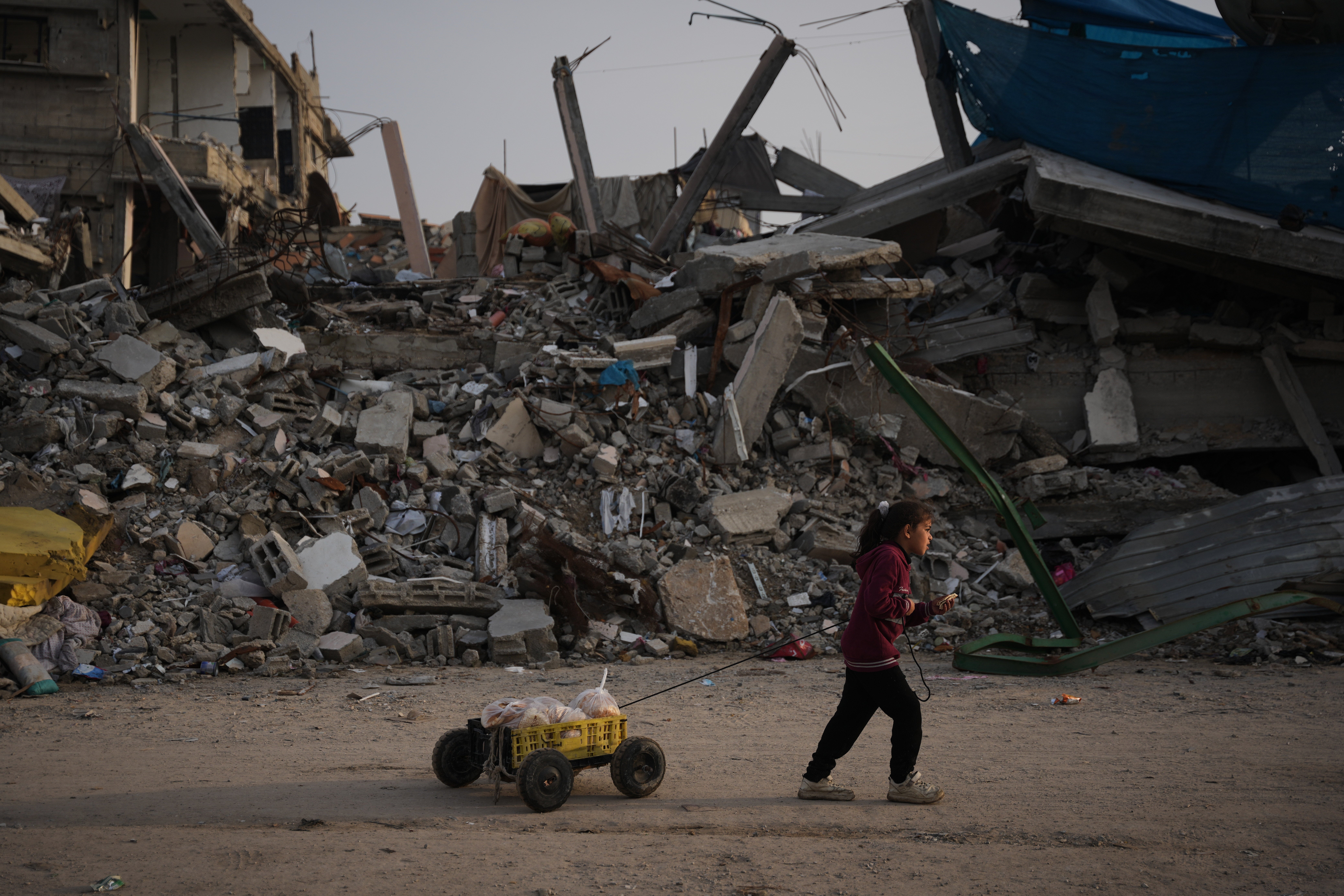 A girl carries bread as she walks past destruction left by Israeli air and ground operations in Gaza City Saturday, Nov. 29, 2025. (AP Photo/Abdel Kareem Hana)