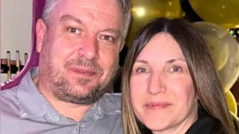 Family photo A man with dark hair and a beard in a grey shirt next to a woman with long brown hair and a dark top