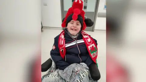 Family handout Kyle, sitting in a wheelchair with a Wales scarf wrapped around him.