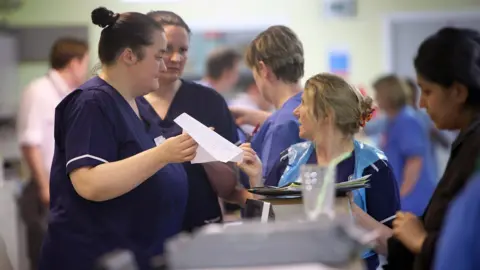 Getty Images File photo shows nurses and doctors chatting and looking at paper documents in a busy hospital corridor on the ward at Selly Oak hospital in Birmingham in 2010.