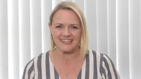 Fiona Graham Dr Graham is smiling at the camera. She has shoulder length blonde hair, with blue eyes and is smiling at the camera. She is wearing a pin-striped grey and white top.