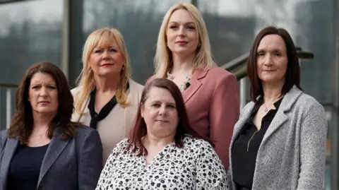 PA Media Five women stand outside a court building. They are standing on steps and, as a result, are seen at different heights. Two are blond, three have dark hair and all their hair is about shoulder-length. They are all smartly dressed - four are wearing jackets (navy, cream, pink and gre) and one is wearing a black and white floral blouse.