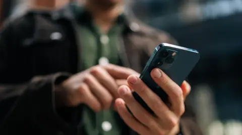 Getty Images A man wearing dark clothes typing on a smartphone.