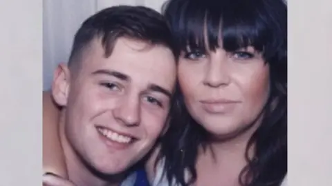 Nicola Howarth A passport-booth style photograph showing Alfie and his mother with their heads close together as they smile at the camera. Alfie has short brown hair, with a curl that falls onto his forehead. Nicola has black, wavy hair, with a heavy fringe. 