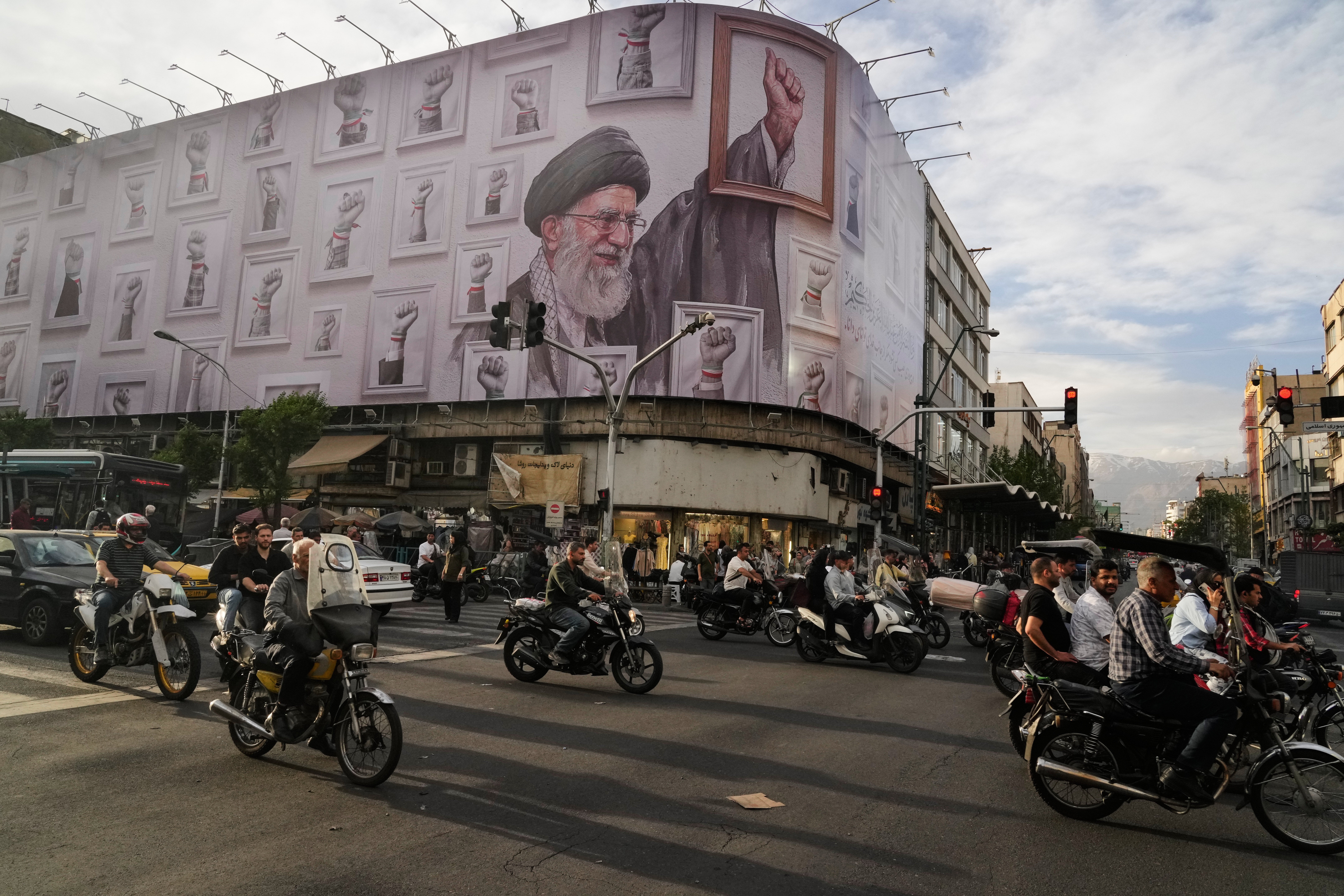 Motorbikes drive past a billboard with graphic showing the late Iranian Supreme Leader Ayatollah Ali Khamenei, who was killed in the U.S. and Israel strikes on Feb. 28, with his framed fist amongst his supporters framed fists in downtown Tehran, Iran, Wednesday, May 6, 2026. (AP Photo/Vahid Salemi)