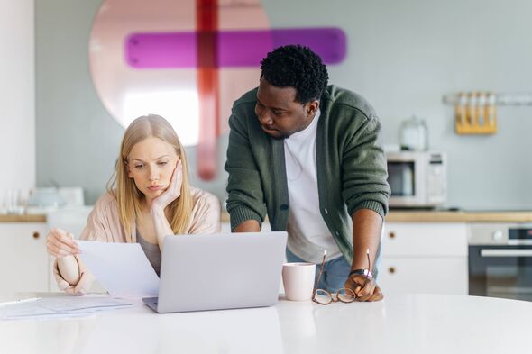 Young adult couple reviewing financial documents and using a laptop in a modern kitchen setting, looking stressed while discussi