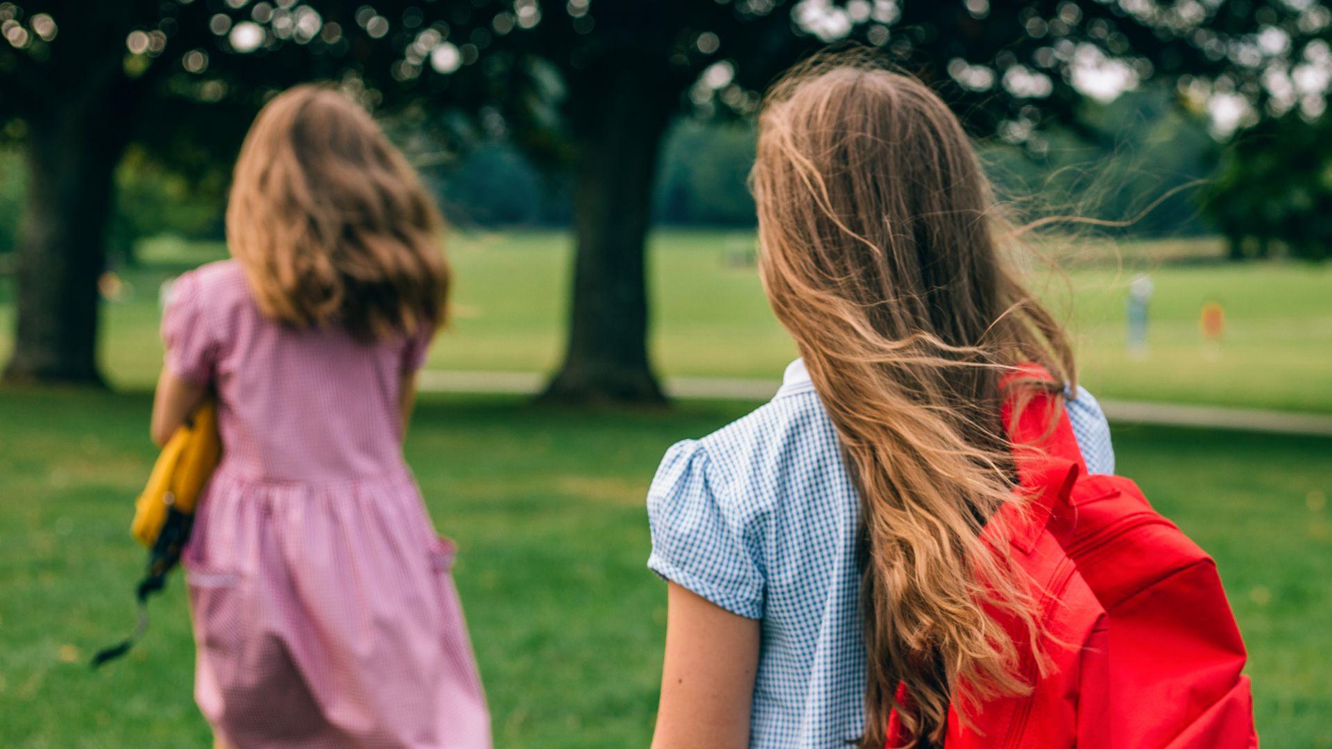 Two children in girls in school uniform walk through a park
