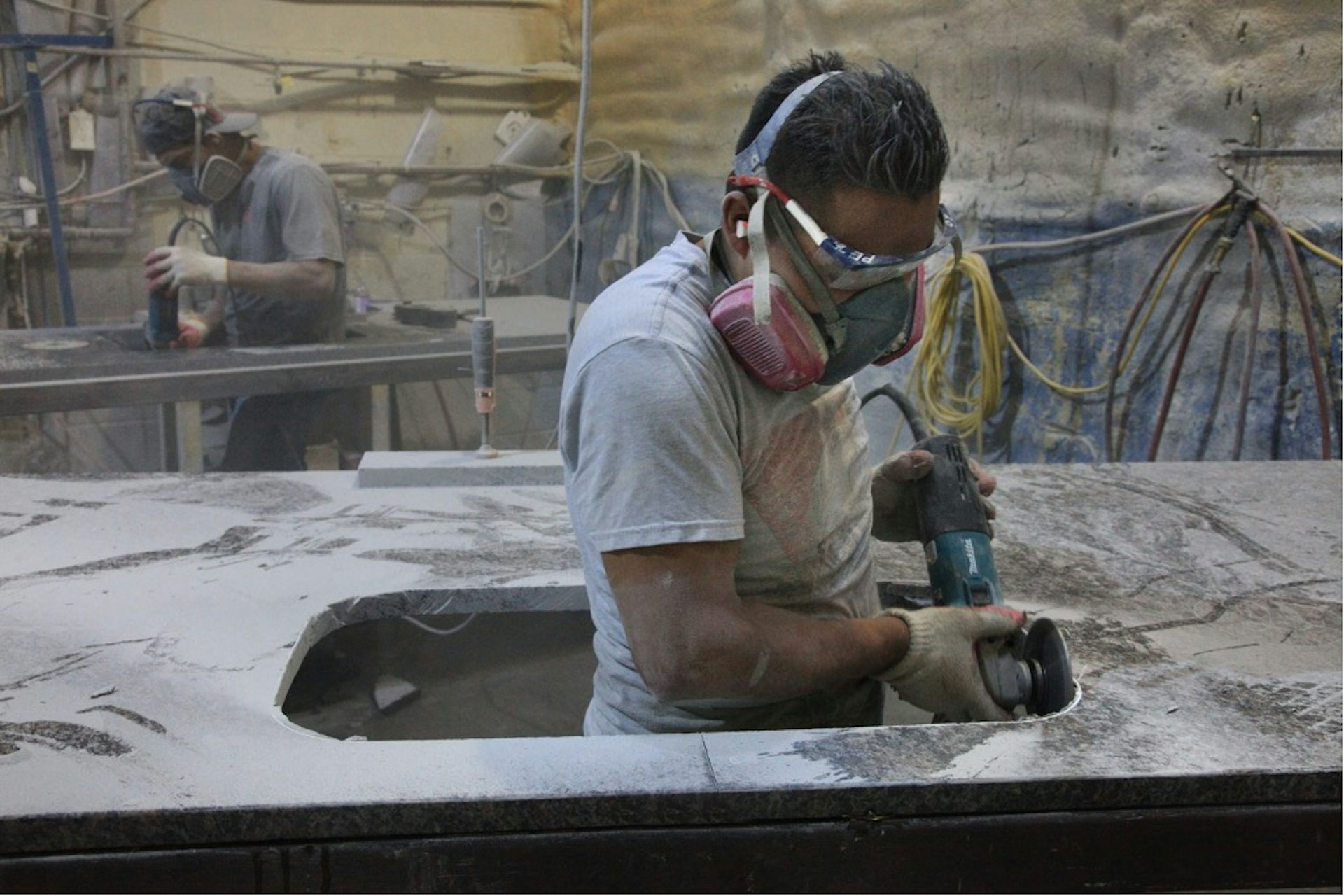 Worker wearing dust mask and grinding a slab of engineered stone.