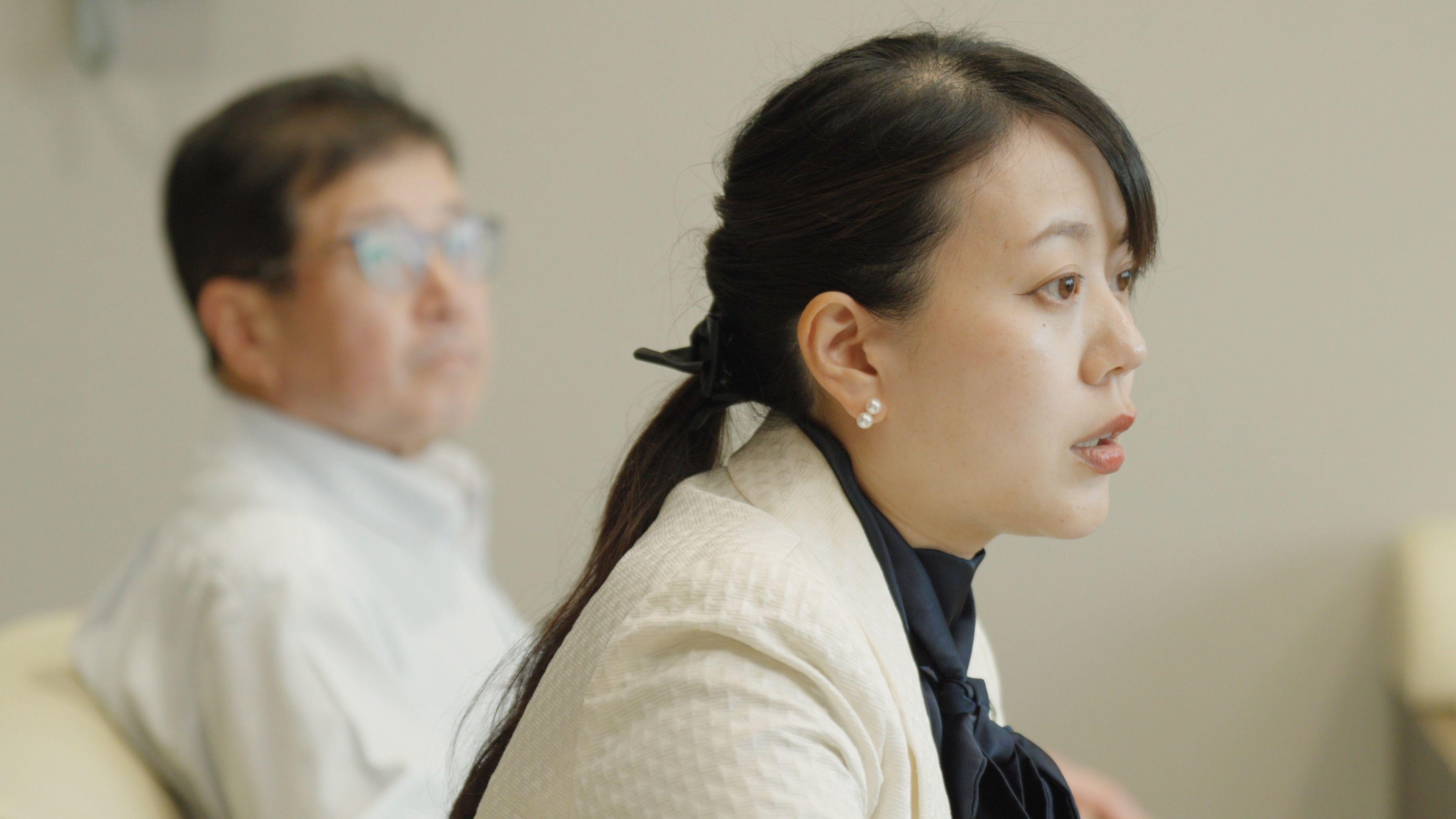 Shoko Kawata, a female mayor in a white blazer and dark blouse sits on an armchair. Her deputy in a light-coloured shirt is visible behind her.