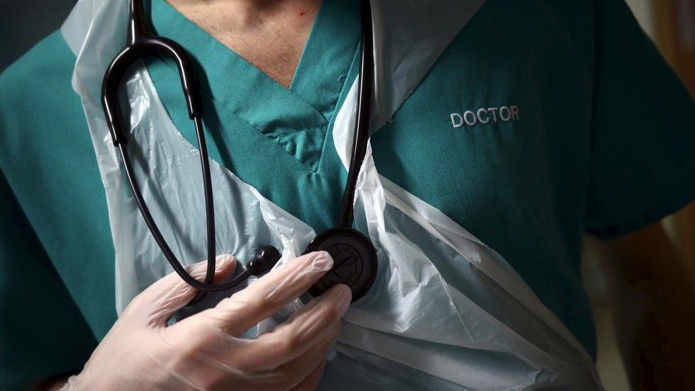 A doctor in green scrubs holding a stethoscope.