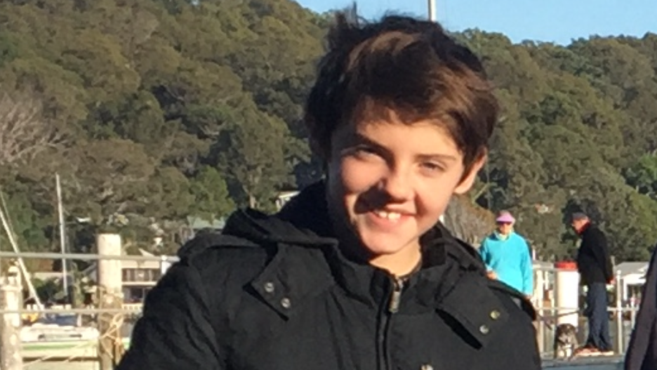 A young by with dark hair smiles at the camera