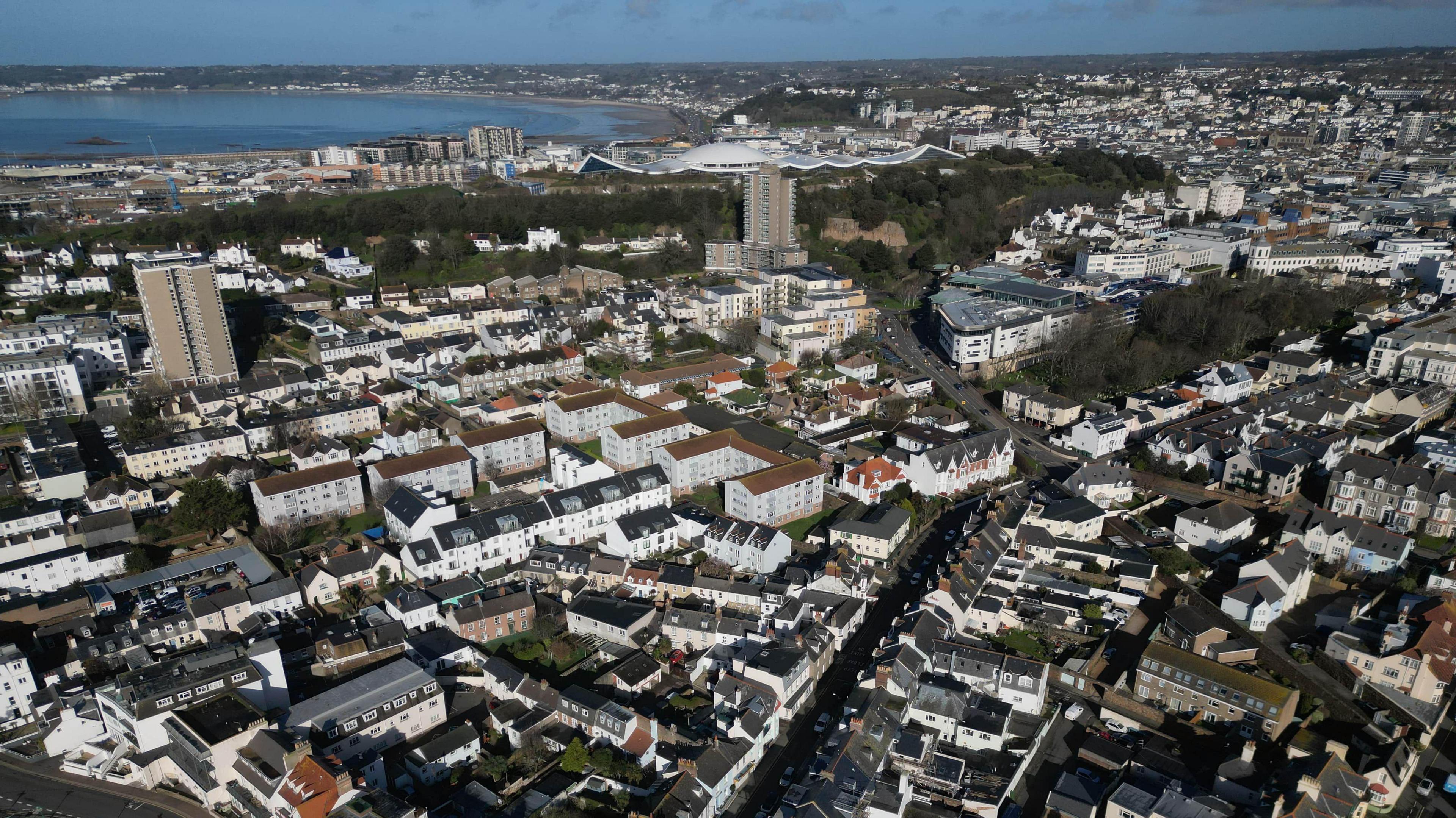 An aerial shot of houses in South St Helier in Jersey in the Channel Islands. A mixture of houses and larger blocks of flats with a number of roads in between. The sea is also in the background.