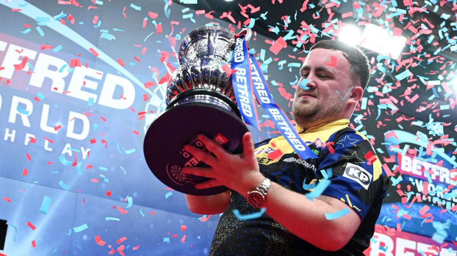 Luke Littler celebrates beating Gerwyn Price in the World Matchplay final at Winter Gardens in Blackpool by lifting the trophy as blue and red confetti drops down