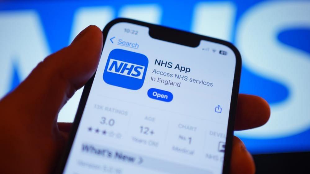A hand holds a smartphone displaying the NHS app after it has been downloaded.