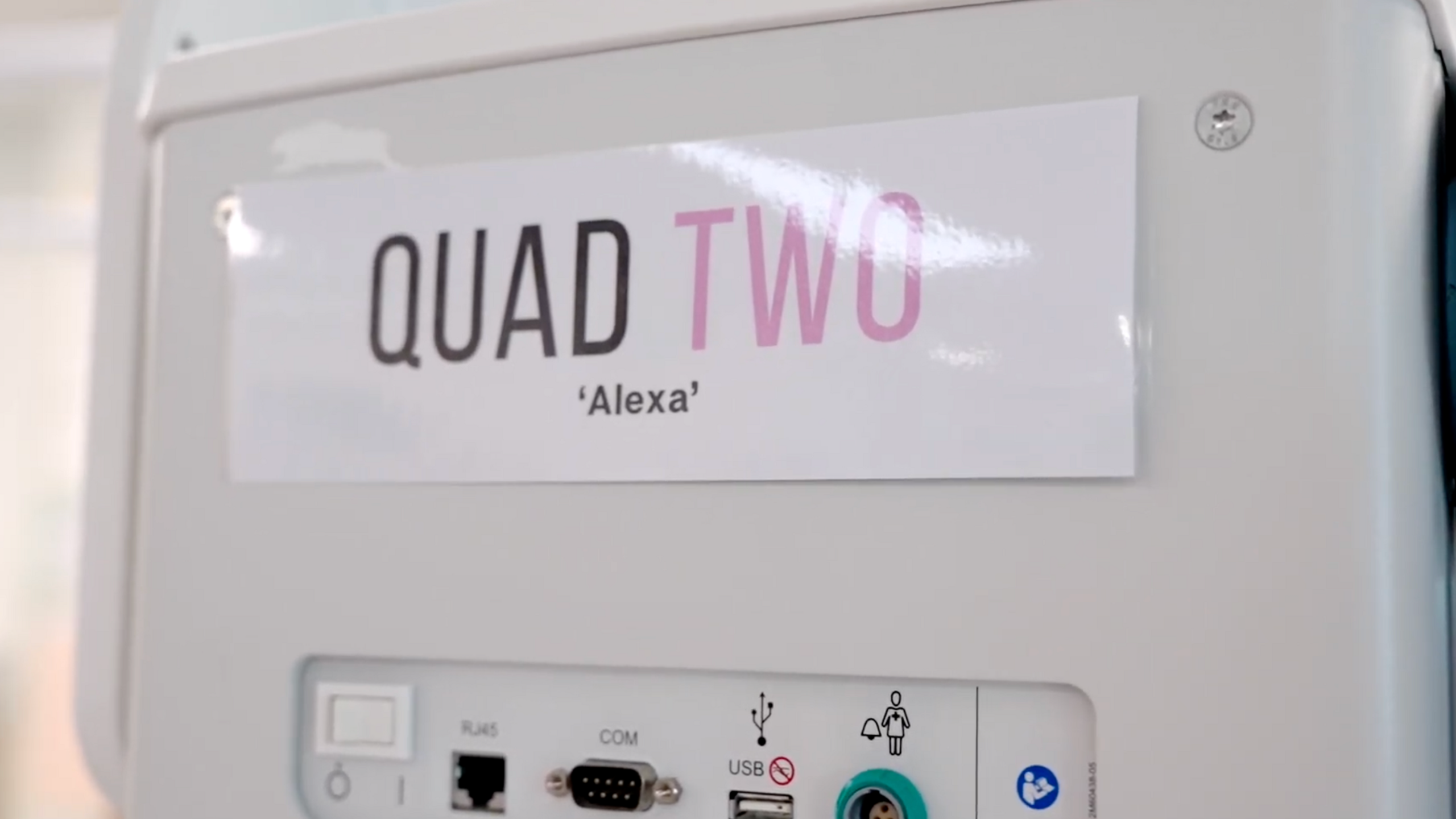 The side of a baby incubator with a laminated sign attached to it that reads 'Quad Two 'Alexa''