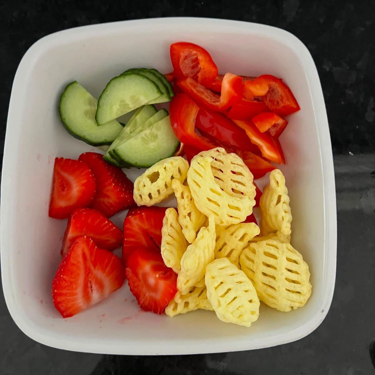 Strawberries, cucumber, peppers and some crisps in a white snack bowl