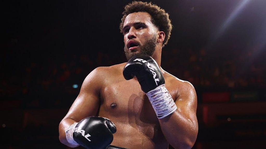 Moses Itauma holds up his hands and is wearing black boxing gloves