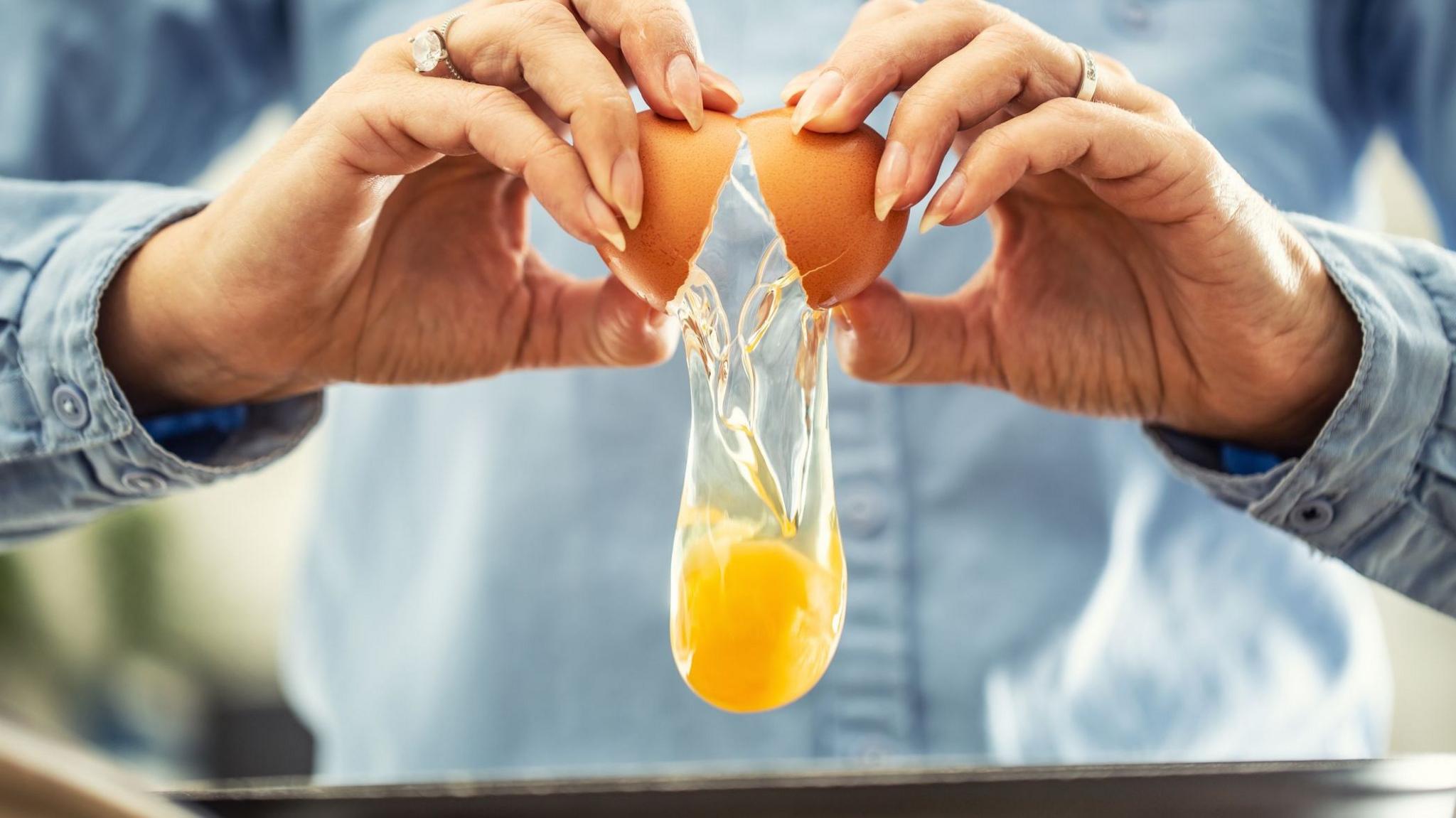 A woman cracks open an egg.