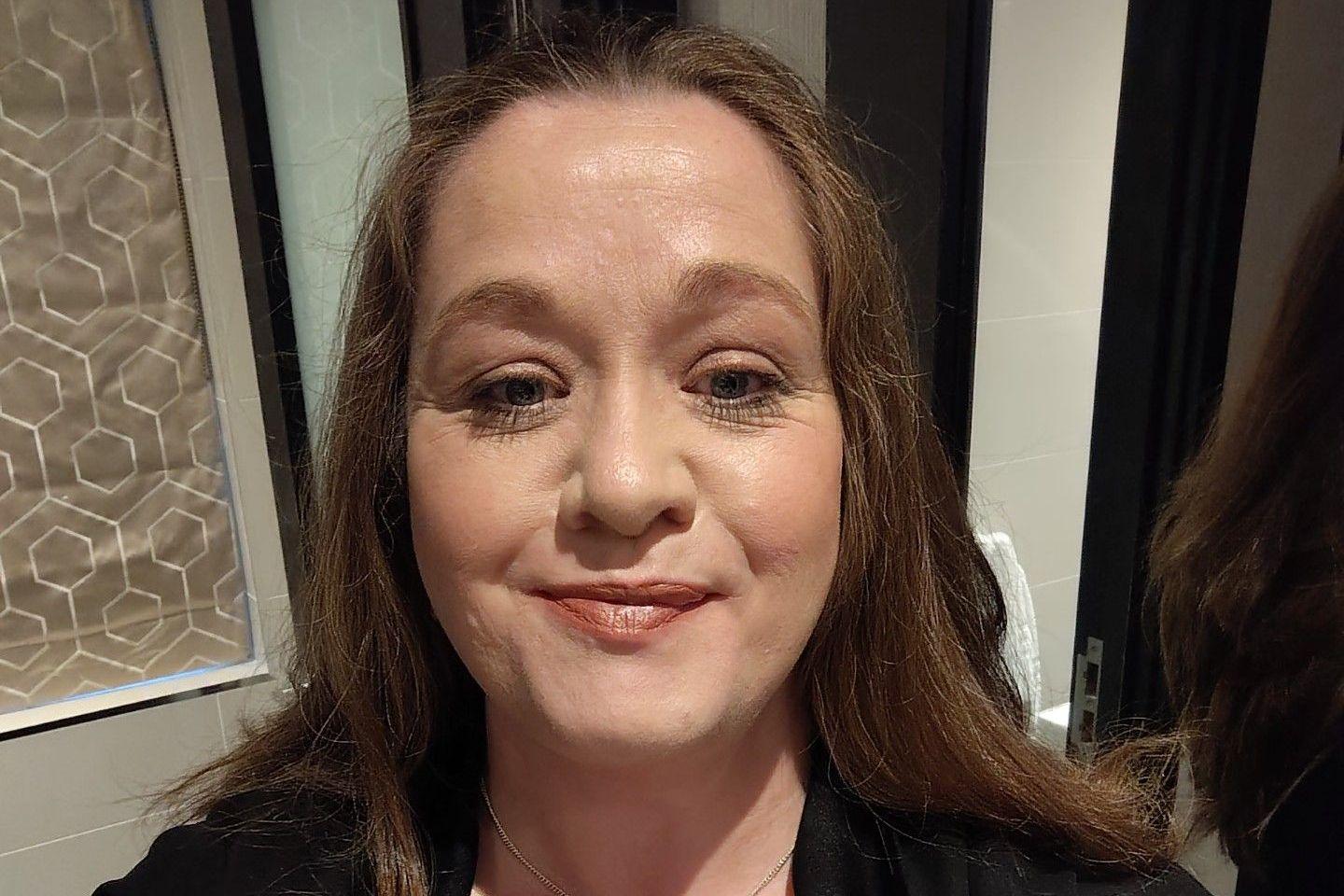 A selfie of a woman with long brown hair. She is smiling at the camera.