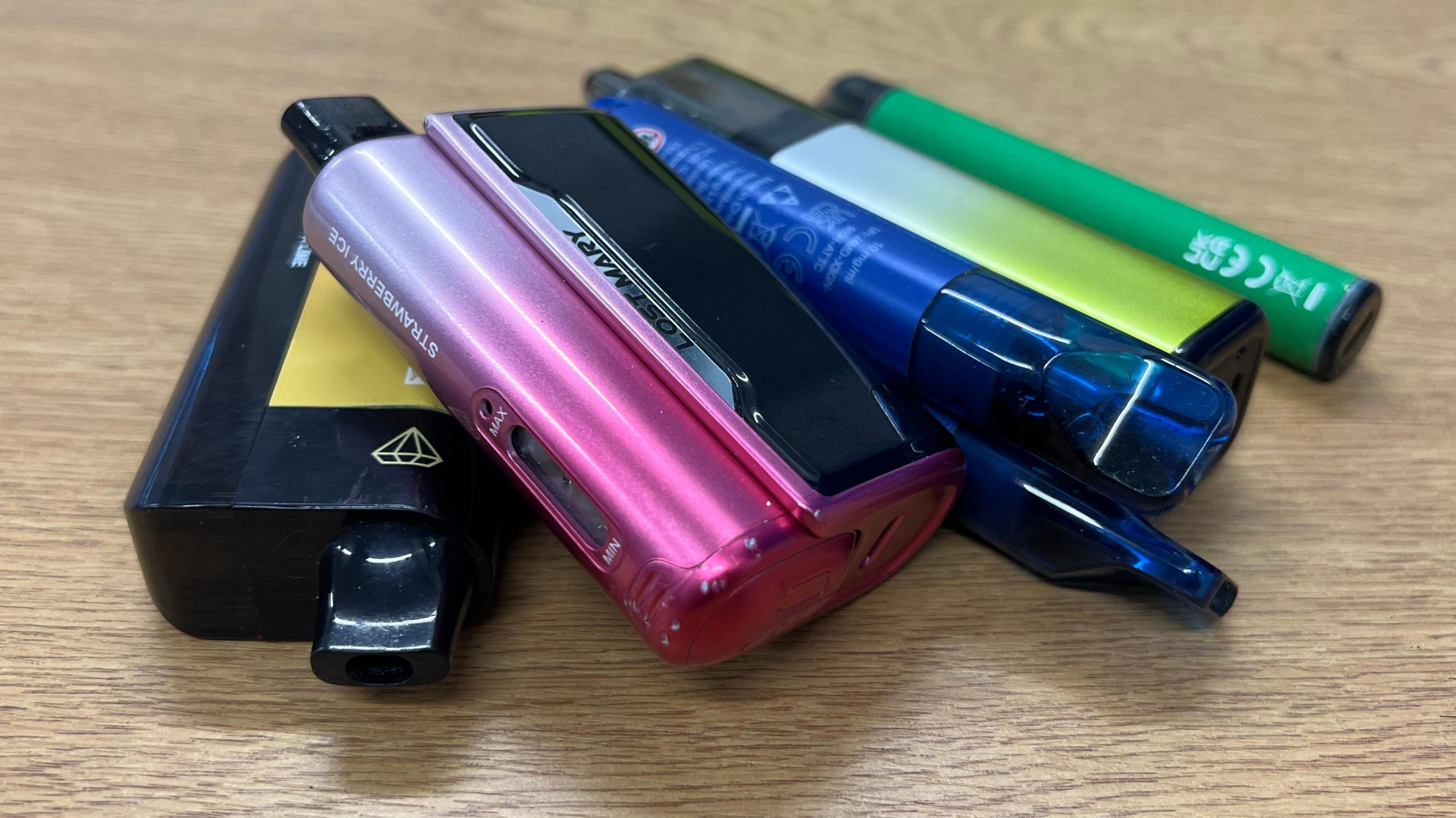 A pile of disposable vapes on a table. They are 