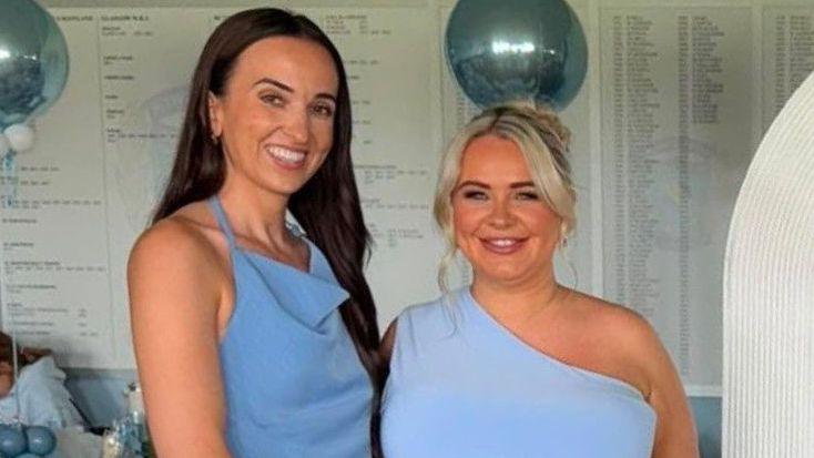 Chelsea McGillivray and Lorna McGillivray. They are wearing blue dresses and smiling at the camera. There are blue balloons in the background.