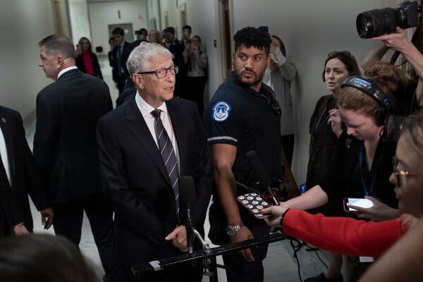 Mr. Gates, wearing a dark suit, speaks to reporter in a hallway.