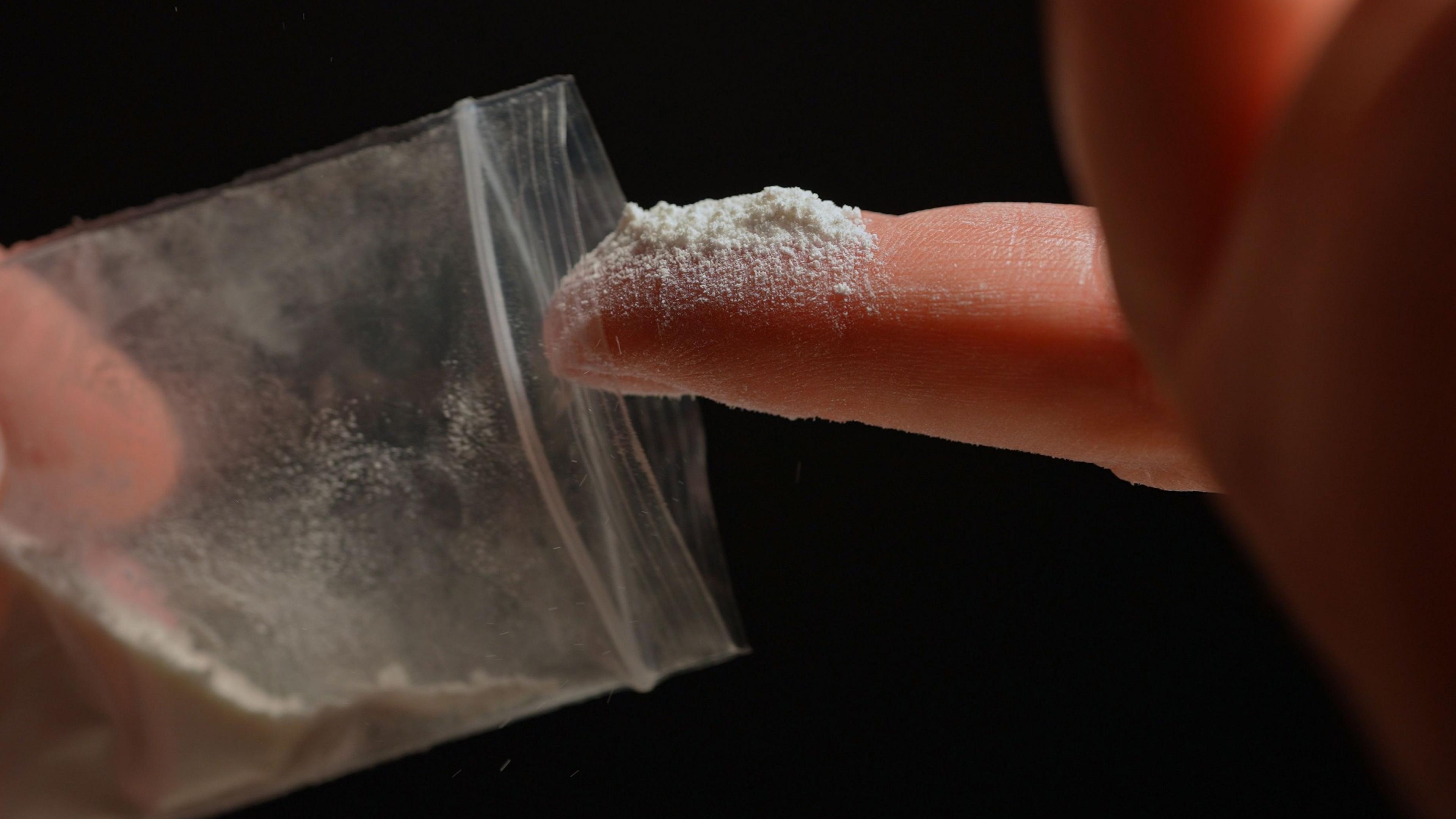 A person has just dipped a finger into a bag containing some off-white powdered drugs.