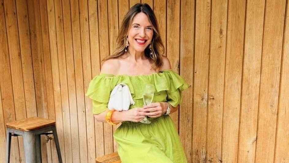 Anna-Louise Dearden sits on a bar stool. She is wearing a lime green dress and is smiling at the camera. 