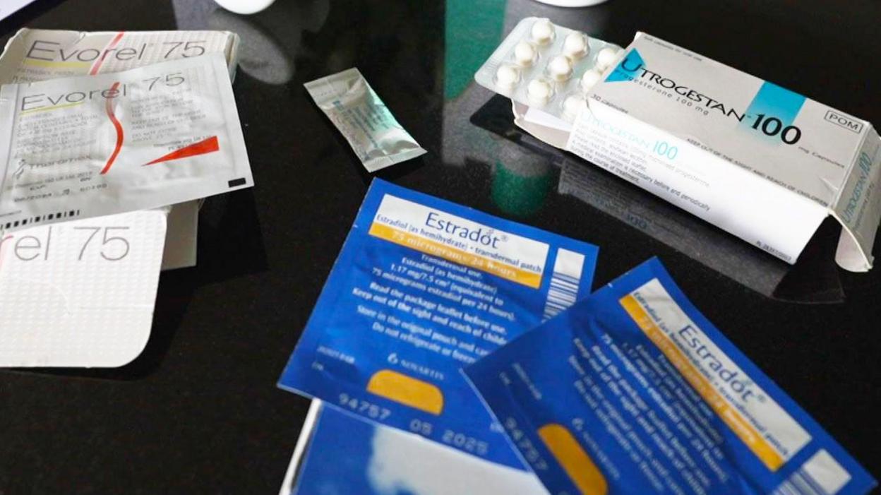 Different types of HRT are laid out on a table, including tablets, patches, spray and gel. In the centre is a small sachet of testosterone gel.