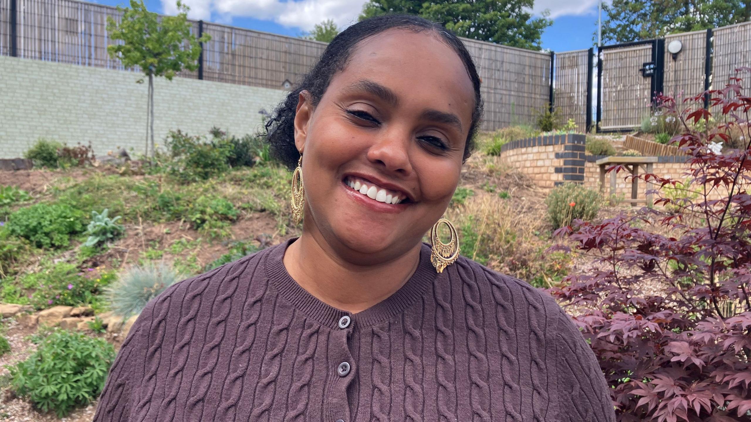 A woman in a brown cardigan stood outdoors smiling at the camera