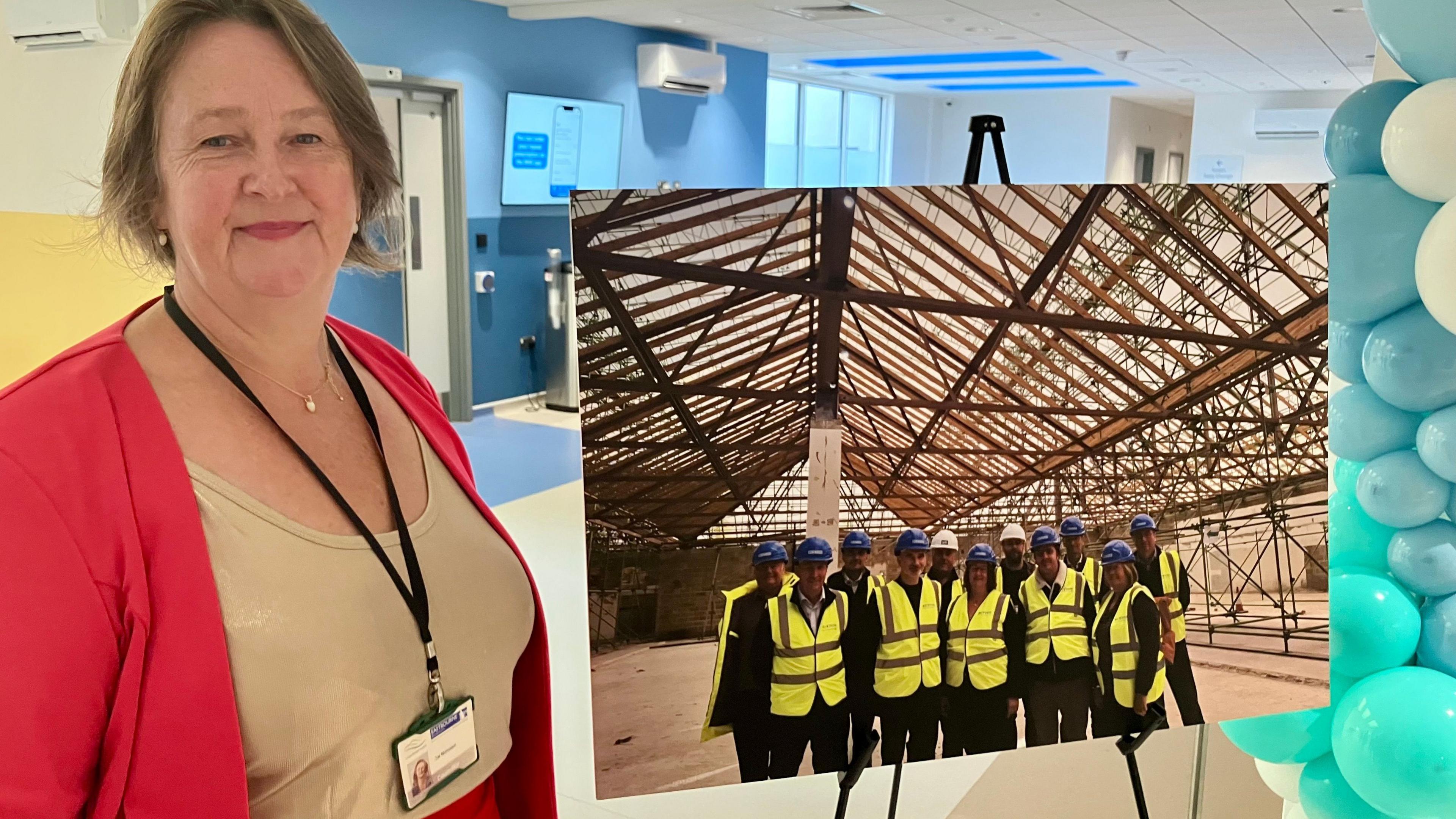A woman in a red jacket stands alongside a large photograph of people in high vis jackets on a building site