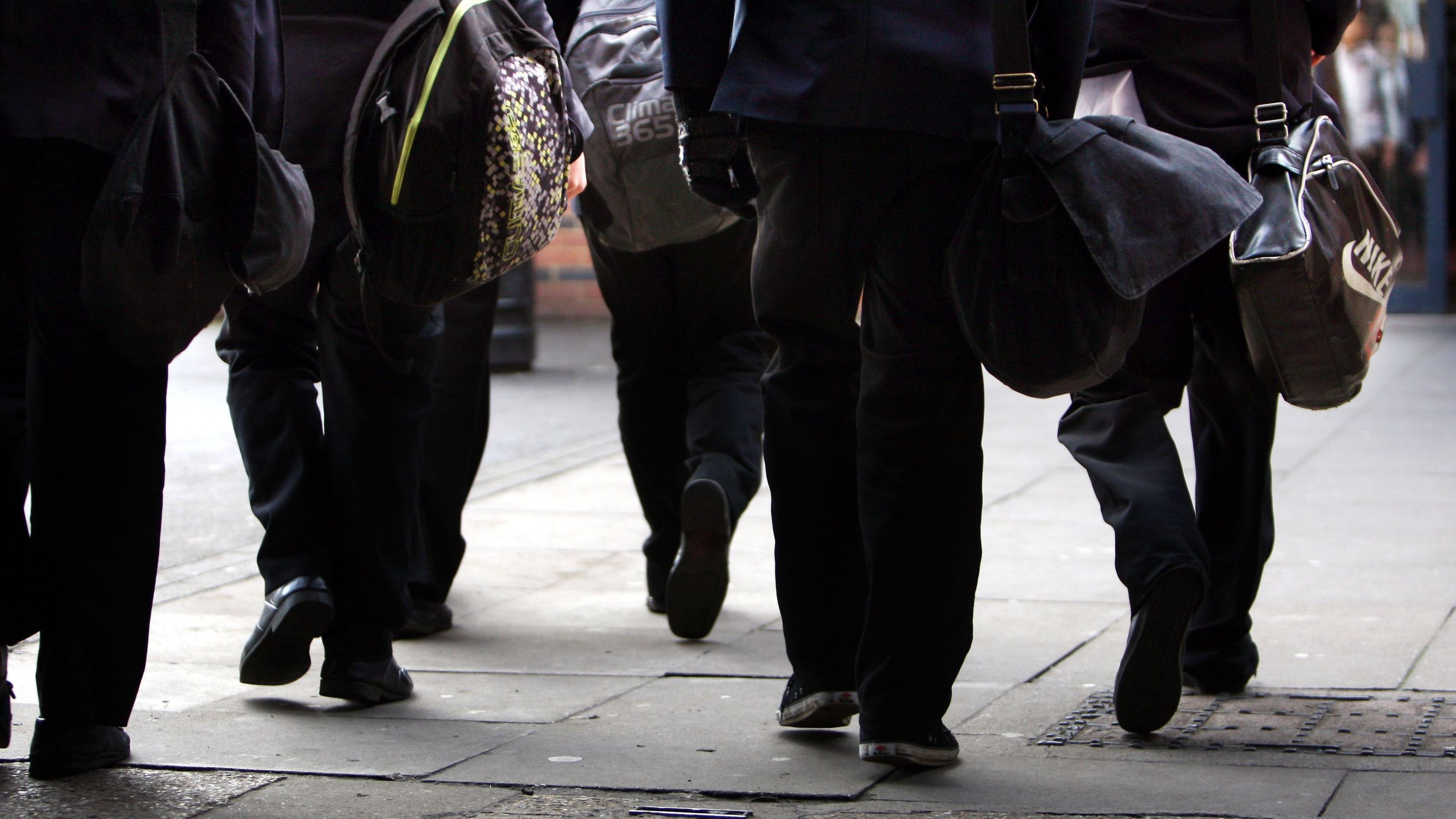 Generic image of school pupils walking. The image shows the legs and shoes of schoolchildren in their uniforms. They are carrying school bags.