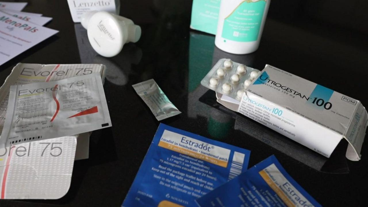 Different types of HRT are laid out on a table, including tablets, patches, spray and gel. In the centre is a small sachet of testosterone gel.